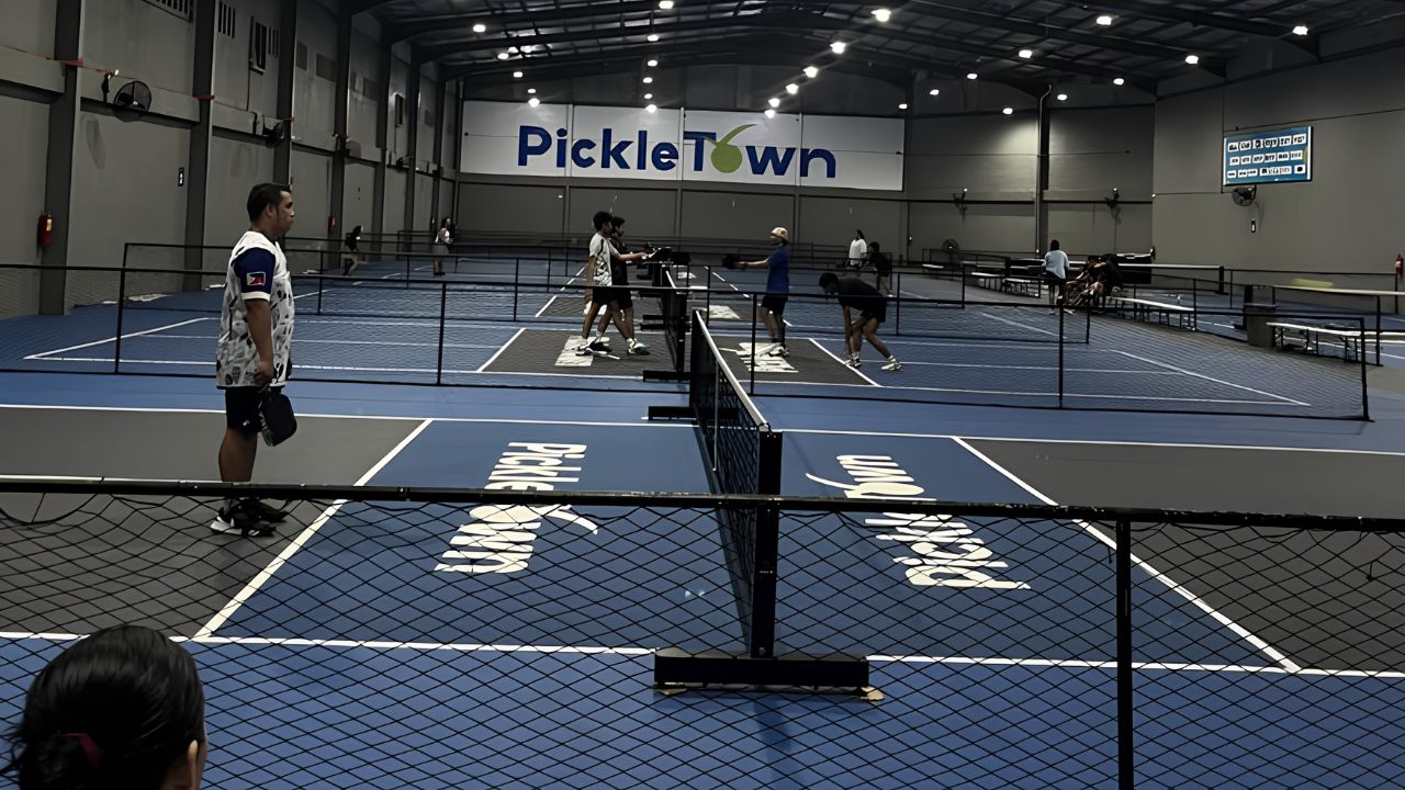 Cụm sân Pickleball trong nhà quy mô lớn, nhiều sân liền kề, mặt sân xanh đậm - xám, có hệ thống chiếu sáng và hàng rào ngăn cách.