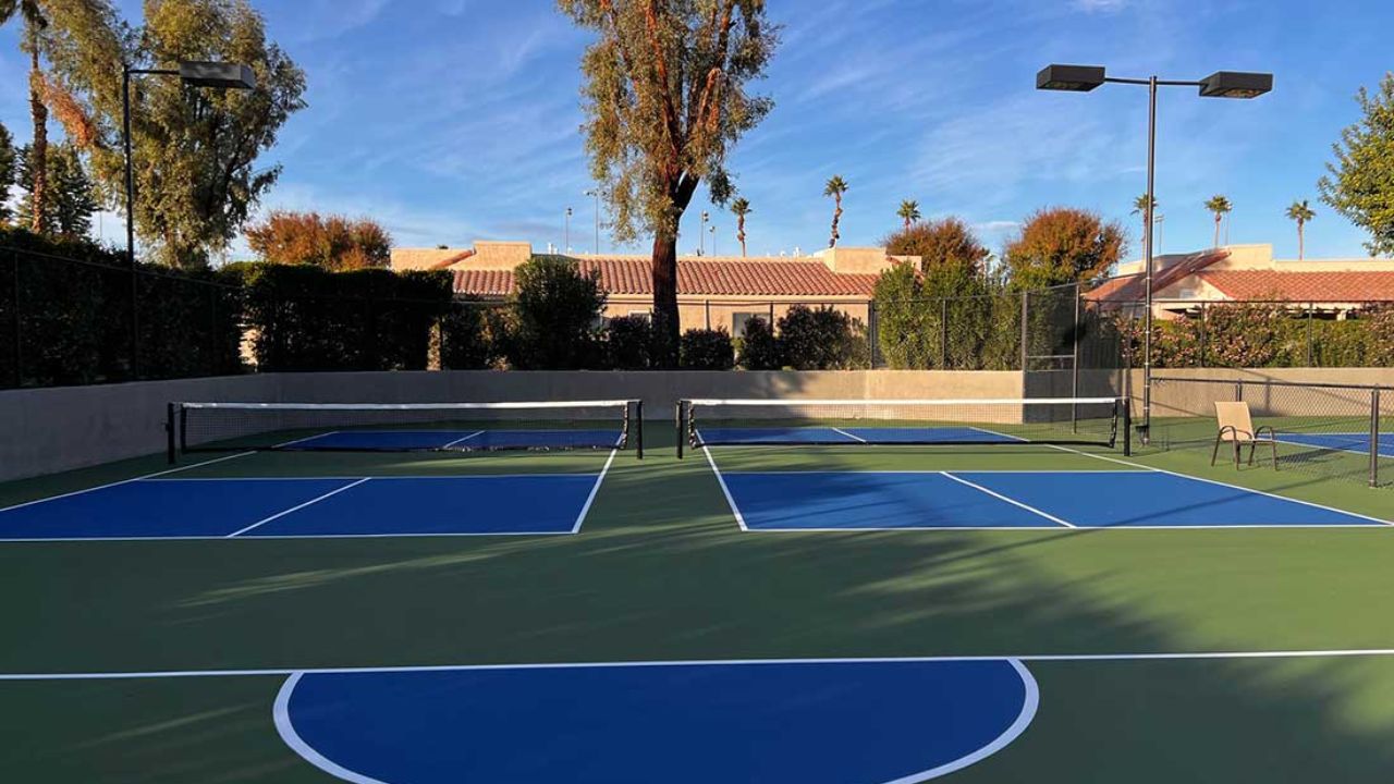 Cụm sân Pickleball ngoài trời gồm nhiều sân liền kề, mặt sân xanh - xanh đậm, có hàng rào, đèn chiếu sáng và cây xanh bao quanh.