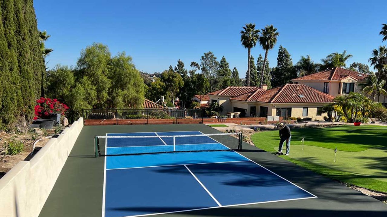 Sân Pickleball ngoài trời nằm trong khuôn viên biệt thự, bao quanh bởi cây xanh và sân cỏ, thiết kế mặt sân xanh - xanh đậm với đường kẻ trắng rõ nét.